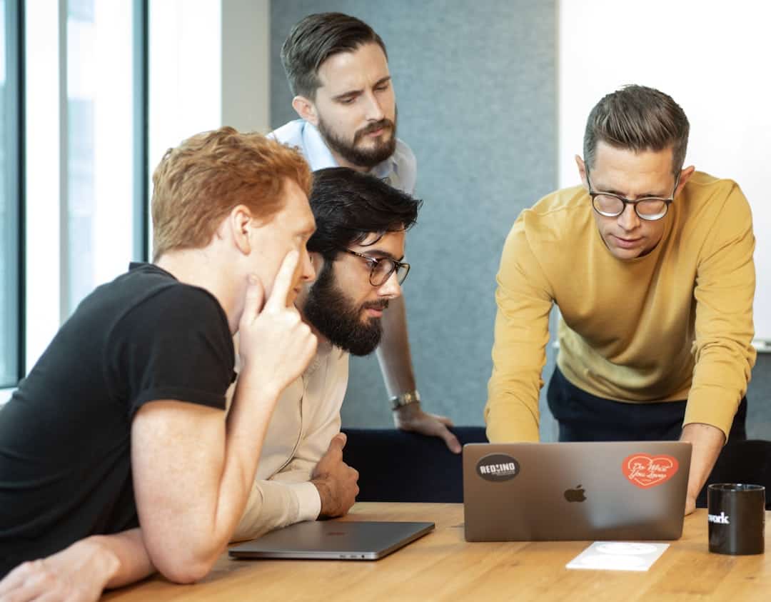a group of men sitting around a table looking at a laptop - change management ai adoption