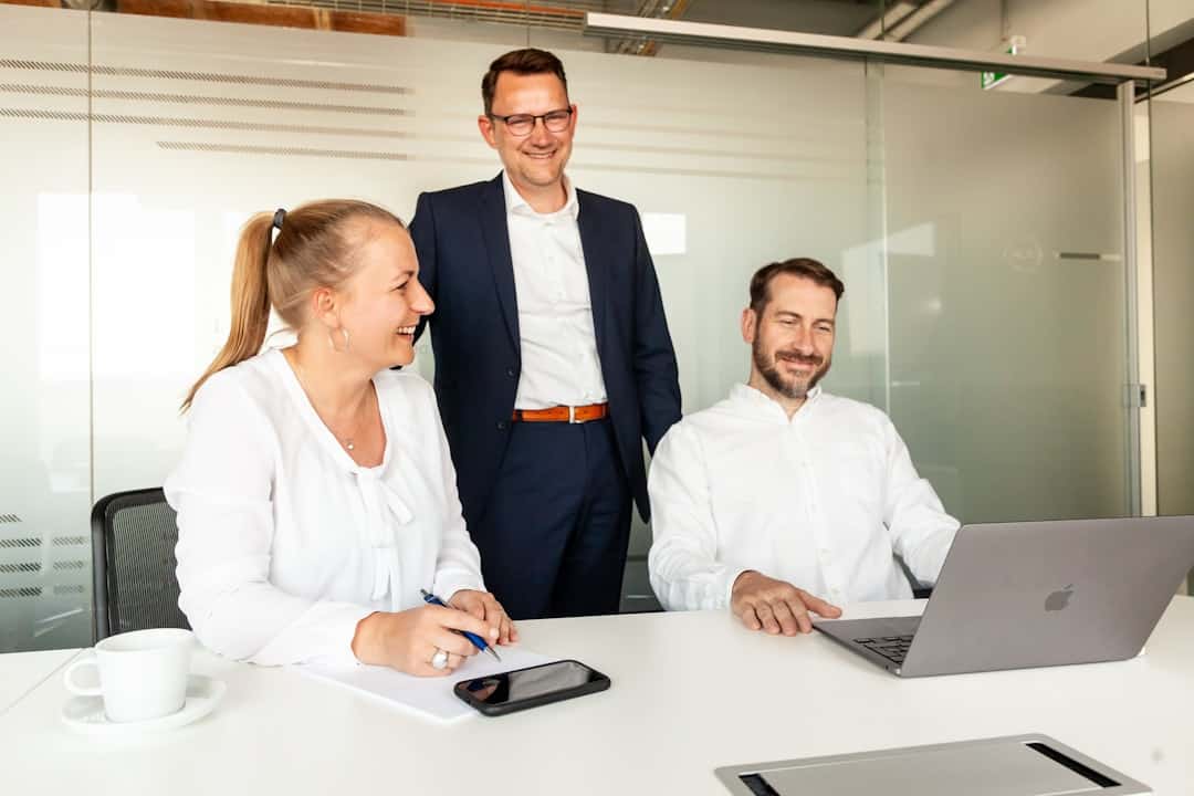 Three colleagues collaborating around a laptop in an office. - ai transformation consulting