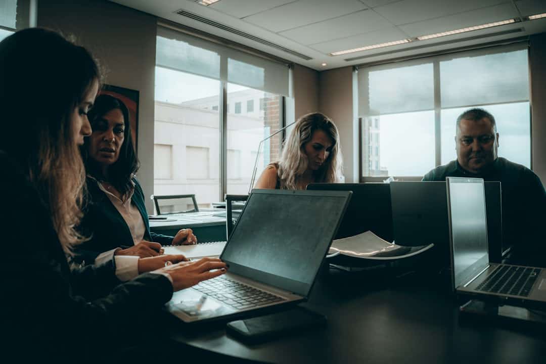 a group of people sitting around a table with laptops - shadow AI governance